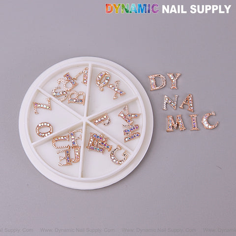 A round case holds 26pcs rose gold AB rhinestone letter charms A-Z; “DYNAMIC” is spelled with these nail charms.