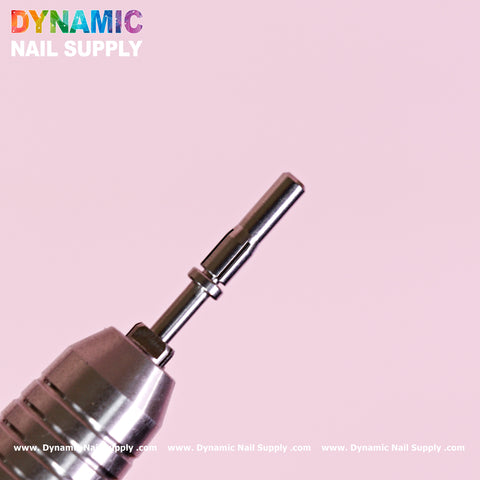 Close-up of a metal drill bit and a Small 3.5mm Easy-Off Mandrel for Smaller Sanding Band against a light pink background. The drill bit glistens with its smooth, cylindrical form. "Dynamic Nail Supply" is positioned in the top-left corner, while the website URL is subtly repeated along the bottom border in small, white text.