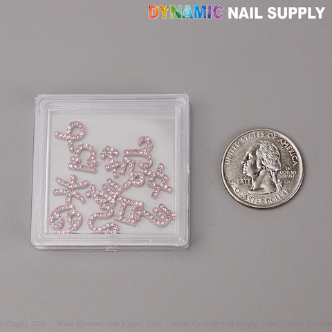 A clear box of 12 pink rhinestone zodiac sign nail charms sits by a U.S. quarter on gray background.