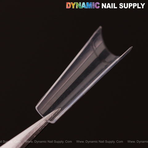 A clear, curved Medium Coffin Nail Tip (Half Cover) held by tweezers; Dynamic Nail Supply logo at top right.
