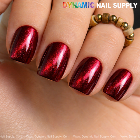 A hand with short nails in glossy Bordeaux Cat Eye #2 gel polish holds a beaded ring; Dynamic Nail Supply above.