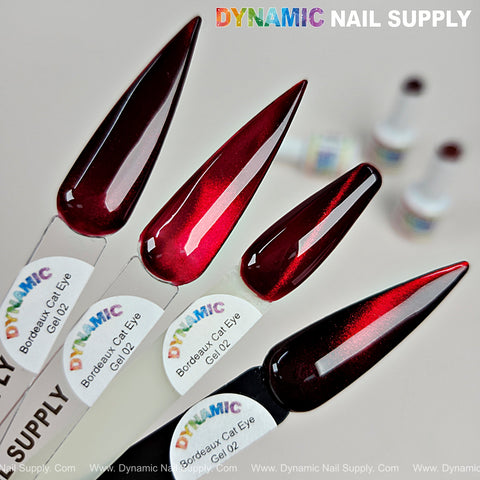 Four pointed nail tips display Bordeaux Cat Eye #2 shimmery glassy red wine gel, with blurred bottles in the background.