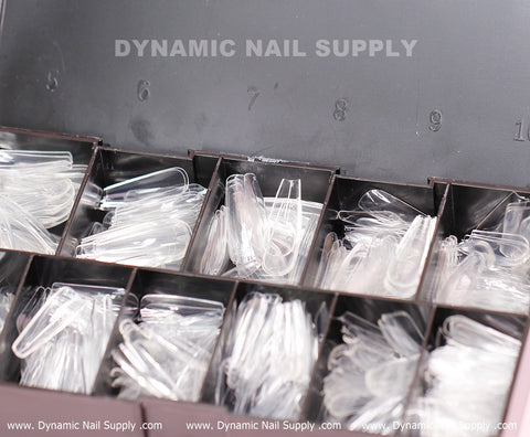 The [Coffin L] Full Cover Tips - Soft Gel X tips - 600 pcs - Box by Dynamic Nail Supply features transparent nail tips, including soft gel options, organized into clearly marked compartments numbered 0 to 9. The Dynamic Nail Supply branding is displayed in white text on the lid, and the base of the box repeats www.DynamicNailSupply.com in small print.
