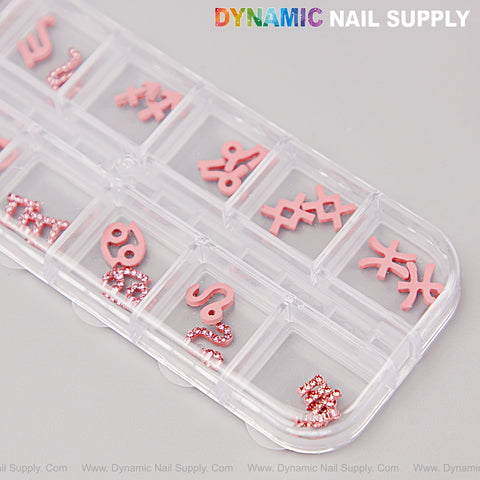 A clear organizer holds 24 pink rhinestone zodiac sign nail charms and DIY design accessories on a light gray surface.