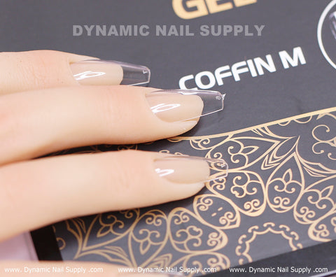 A hand with long nude coffin nails holds a black and gold box of Coffin M Full Cover Tips, Soft Gel X, 600 pcs.