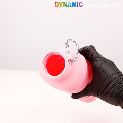 A gloved hand holds a Collapsible Silicone Lightweight Reusable Pink Bottle with a metal carabiner, top open.