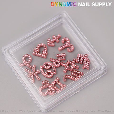 A clear case holds 12 pink rhinestone zodiac sign charms for nail art DIY, under the Dynamic Nail Supply logo.