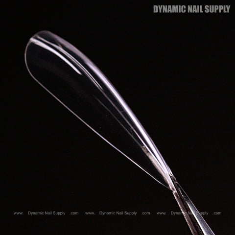 A Sculpted Stiletto XL Full Cover Soft-Gel Nail Tip (Black Box) is displayed on a stick against a black background.