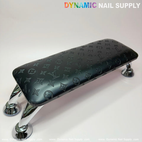 A stylish black rectangular armrest adorned with an LV monogram pattern, supported by sleek chrome legs, is perfect for enhancing any manicure nails service. It elegantly pairs with a leather pillow cushion and features the brand name Dynamic Nail Supply at the top of the image.