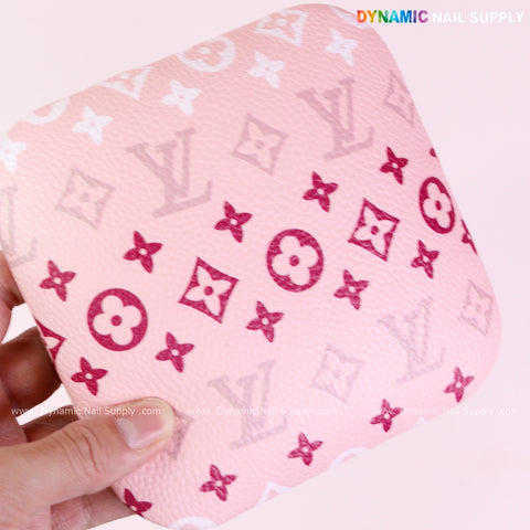 A hand holds a pink (RA018) Elbow Armrest for Nail Technicians with LV-inspired patterns and a textured surface.