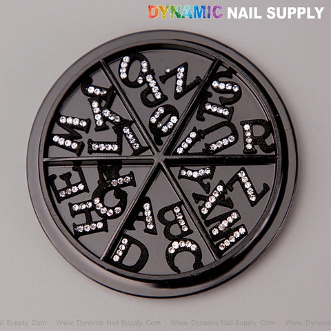 A black round wheel holds 26pcs silver rhinestone letter nail charms, A-Z, in separate wedge compartments.
