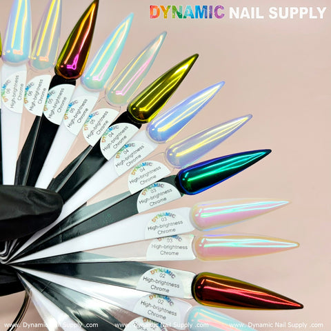 A collection of multicolored, iridescent nail polish samples, treated with high brightness fine pigment powder, is showcased on white swatches held by a hand clad in a black glove. The vibrant nails, featuring shades of blue, green, red, gold, and silver from the Orange/Gold/Mermaid Iridescent Chrome #06 set by Dynamic Nail Supply—perfect for any nail art enthusiast—are complemented by the DYNAMIC NAIL SUPPLY branding visible at the top.