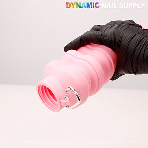 A black-gloved hand holds a Collapsible Silicone Lightweight Reusable Pink Bottle for liquid, travel, or hiking.