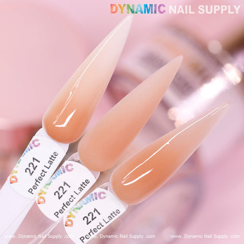 A close-up of three pointed nail samples in shades of neutral and pinkish-latte, expertly crafted with long-lasting, non-toxic Perfect Latte - Nude Acrylic Powder (#221) from Dynamic Nail Supply. Each sample is labeled 221 Perfect Latte. The background showcases a blurred image of a nail product container with Dynamic Nail Supply's logo prominently displayed at the top.