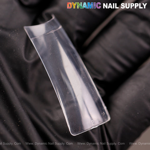 A gloved hand holds an XXL Duck Shape Nail Tip with DYNAMIC NAIL SUPPLY at the top right corner.