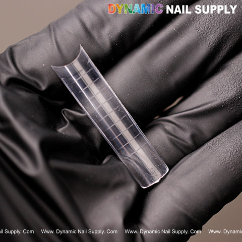 A gloved hand holds XXL Square Clear Nail Tips with lines; 500pcs, 10 sizes by DYNAMIC NAIL SUPPLY shown above.