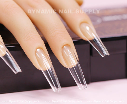 Close-up of a mannequin hand showcasing the [Coffin XXL] Full Cover Tips from Dynamic Nail Supply. These extra long, clear coffin-shaped soft gel X tips feature a highly glossy, transparent finish that seamlessly extends from the natural-looking nail bed. Elegantly resting on a black surface, the image includes text: Dynamic Nail Supply.