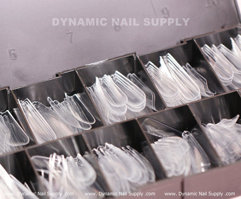 The plastic organizer box features several compartments containing clear, plastic nail tips, including extra long coffin shaped options. Each compartment is filled with tips in a variety of sizes. The lid of the box prominently displays the brand name Dynamic Nail Supply, and their website www.DynamicNailSupply.com is printed at the bottom of the image. This set includes 360 pieces of [Coffin XXL] full cover soft gel X tips in 11 different sizes.