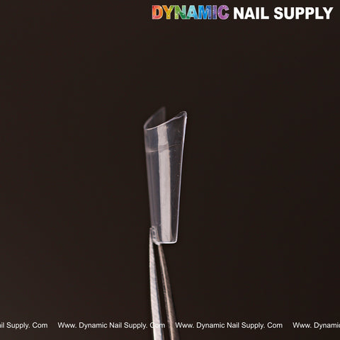 A clear New Short Coffin Nail Tip Half Cover (600 pcs, 12 sizes) held by tweezers on a dark background.