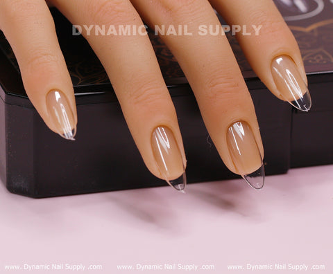A mannequin hand featuring glossy nails adorned with Medium Almond Shape Full Cover Tips is displayed on a black surface. The nails have a natural beige base, while "Dynamic Nail Supply" is gently visible at the top and along the bottom edge of the image, creating a subtle visual harmony.