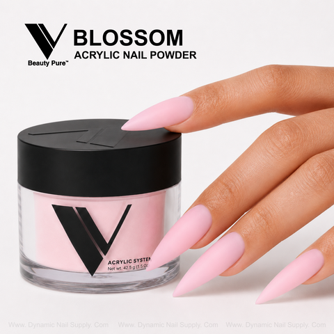 Hand with long, pointed, nude-pink acrylics next to a V Beauty Pure - Blossom Acrylic Powder jar on white background.