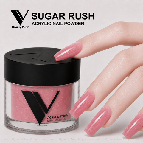 A hand with long pink acrylics touches a V Beauty Pure - Sugar Rush Glittery Acrylic Powder jar on a white background.