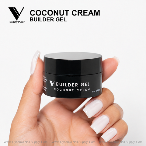 A pale pink-manicured hand holds a black jar labeled Coconut Cream - V Beauty Pure Builder Gel by Dynamic Nail Supply.