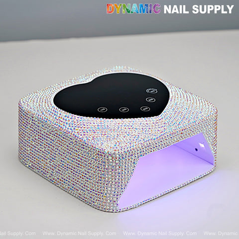 The AB Big Rhinestone UV/LED Cordless 72W Lamp with heart display and auto sensor glows purple on a white surface.