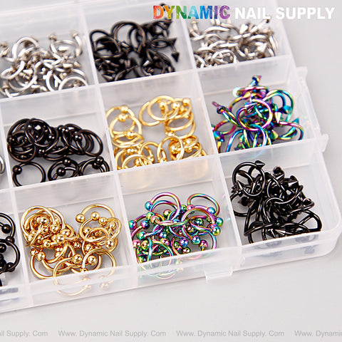 A DYNAMIC NAIL SUPPLY box holds gold, silver, titanium, and black piercing nail charms for Y2K nail art DIY designs.