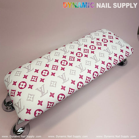 A manicure nails service features a (White Pink LV Pattern) ArmRest with a leather pillow cushion, designed in a luxurious pink and gray pattern. It is complemented by shiny metal legs and showcased against a light pink background, with the brand name Dynamic Nail Supply displayed in the top right corner.