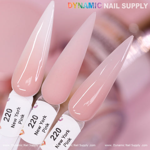Close-up of three elongated, almond-shaped nail tips on a pink background. Each tip showcases the soft pink shade of New York Pink - Nude Acrylic Powder (#220) by Dynamic Nail Supply, known as the best cover color for daily use. These glossy tips, including one with a subtle gradient effect, are elegantly set against the blurred branding of Dynamic Nail Supply.