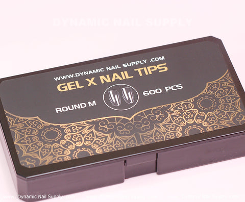 A black rectangular box adorned with intricate gold patterns on the lower half is labeled with "Dynamic Nail Supply's [Round M] Full Cover Tips." It features text indicating 600 pieces of Medium Long Soft Gel X tips in 10 sizes. Adding to its appeal, the website www.dynamicnailsupply.com is prominently displayed at the top against a light pink background, emphasizing their dedication to superior nail products.