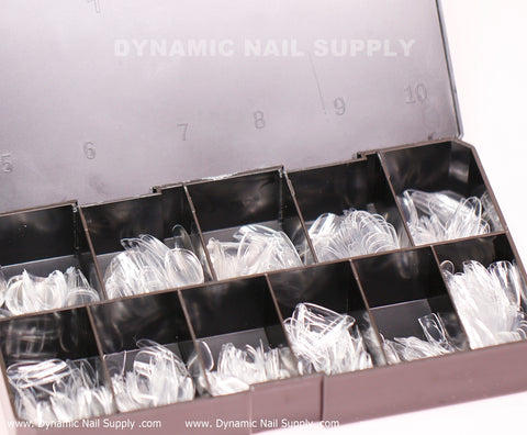 A black plastic storage box with a transparent lid organizes 600 medium-long, full cover soft gel X nail tips from Dynamic Nail Supply. These clear tips are divided into ten distinct compartments, labeled from 0 to 9, with the brand name printed on the inside of the lid.