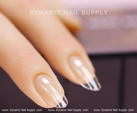 A close-up shot features a hand mannequin adorned with a medium-long, clear nail enhanced with silver tips. Showcasing the [Round M] Full Cover Tips from Dynamic Nail Supply, these nails exhibit a shiny, professional finish. The background is subtly blurred, highlighting the brand name "DYNAMIC NAIL SUPPLY" at both the top and bottom of the image, emphasizing an elegant manicure style.