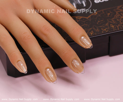 An authentic hand model showcases a set of manicured nails adorned with [Oval] Full Cover Tips, the Soft Gel X tips variety. These nails possess a delicate, glossy finish akin to high-quality acrylic work. The hand is placed on a black box featuring the Dynamic Nail Supply logo, with a pink surface underneath.