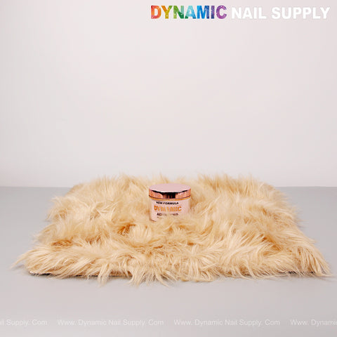 A pink nail powder jar sits on a Tan Faux Fur Fabrics Square Display Mat, with DYNAMIC NAIL SUPPLY text above.