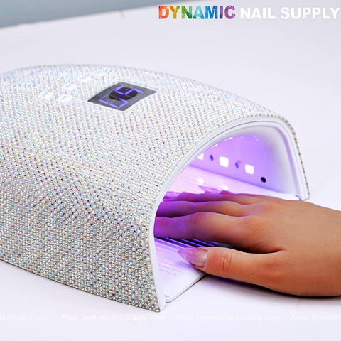 A hand is inside the AB and Pearl Rhinestone Cordless LED/UV 48W Gel Nail Dryer with purple light and digital timer.