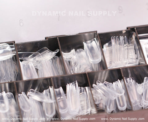 A close-up of a divided box showcasing the [Square L] Full Cover Tips, including Soft Gel X tips from Dynamic Nail Supply. Each compartment organizes different sizes and shapes of full cover tips in a Square Long Shape. The compartments are faintly marked with the Dynamic Nail Supply watermark.