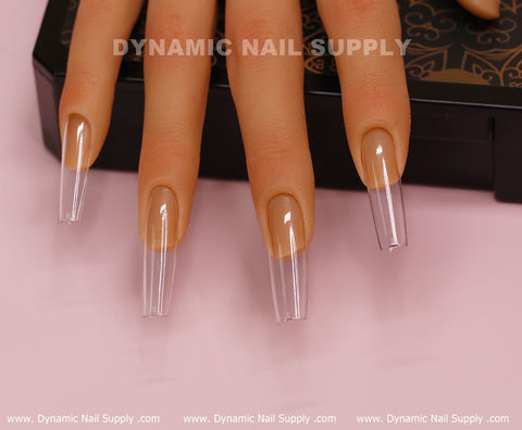A mannequin hand showcases long, glossy soft gel nails featuring the [Square L] Full Cover Tips from Dynamic Nail Supply. The neatly applied nails have a clear, coffin shape, highlighting their smooth, polished finish. Black design elements are present in the background, with the brand name Dynamic Nail Supply prominently displayed at both the top and bottom of the image.