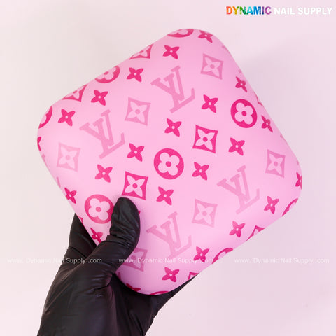 A gloved hand holds a Pink and Pink LV Smooth Leather Elbow Cushion Pad Arm Rest for manicure; DYNAMIC NAIL SUPPLY top right.