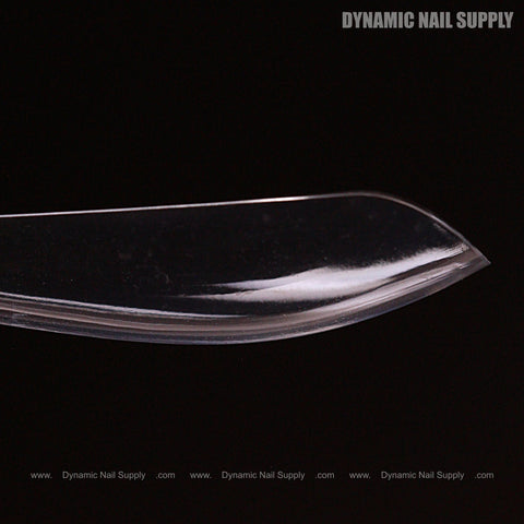 A clear, curved Sculpted Stiletto XL Full Cover Soft-Gel Nail Tip with DYNAMIC NAIL SUPPLY in grey at top right.