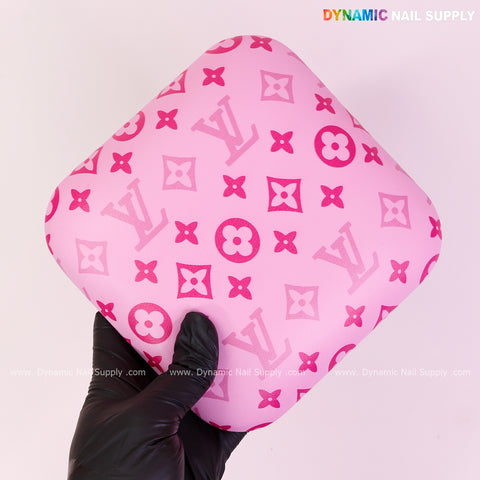 A gloved hand holds a Pink and Pink LV Smooth Leather Elbow Cushion Pad Arm Rest Support for manicure nail desk.