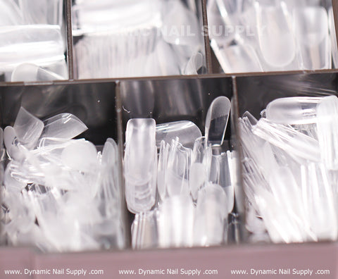A close-up of a Dynamic Nail Supply storage box reveals a variety of Soft Gel X tips. Each compartment is neatly organized with different shapes, including stiletto, almond, and [Square M] Full Cover Tips. Some sections are visibly fuller, reflecting the impressive quantity and diversity offered in this collection of Medium Length Square Nail Tips with 600 pieces across 11 sizes.