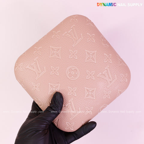 A gloved hand holds a Neutral Skin Color LV Engrave Elbow Pad Pillow for Nail Tech against a light pink background.