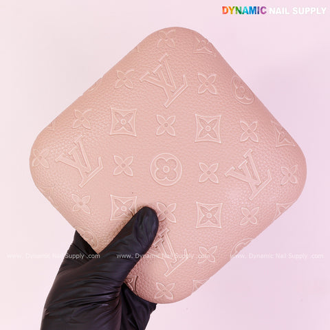 A gloved hand holds a pink pouch by the Neutral skin Color LV Engrave Elbow Pad Pillow for Nail Tech on a pale pink background.