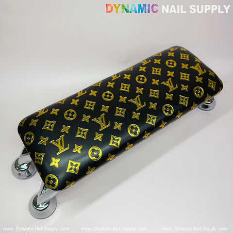 The (Black Gold LV Pattern) Leather Cushion Armrest with Pillow for Manicure Pedicure from Dynamic Nail Supply features a glossy black surface adorned with a luxurious gold monogram pattern. Supported by four chrome legs with rubber tips, it perfectly complements any UV nail light setup.