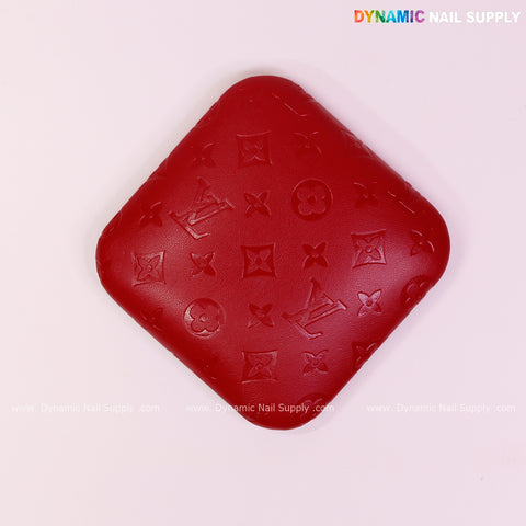 A red LV Engrave Elbow Pad for Nail Tech—soft PU leather, padded, supportive—on a pink surface; DYNAMIC NAIL SUPPLY shown.
