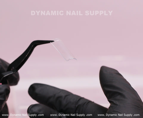 A gloved hand holds XL Square Nail Tips (Not C-Curve), extra long straight, with tweezers on a light pink background.