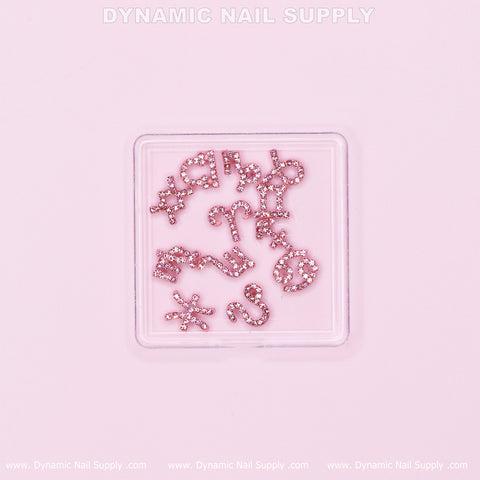 A square container houses the Luxury Light Pink Zodiac Symbol Sign Nails Charm Set with Rhinestone on a pale pink background. The top features "Dynamic Nail Supply," with the text repeated along the bottom edges. Each small, sparkling charm glistens like Rhinestone Birthday Nails, randomly arranged within the container.