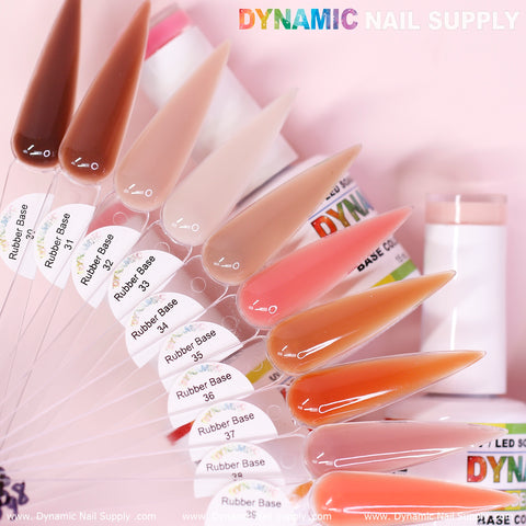 A display showcases elongated nail samples in a range of nude, pink, and orange shades from the (BIAB) Rubber Base Gel (Builder Gel in a Bottle) Number 30 to 39 collection. The background features a white and pink gradient with the Dynamic Nail Supply logo. Partially visible are containers of soak-off gel.